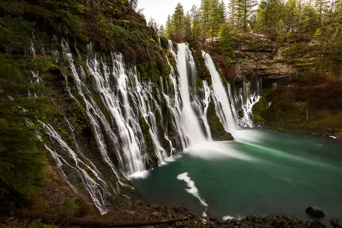 A large waterfall flows down a mossy rock cliff into a pool of green water.