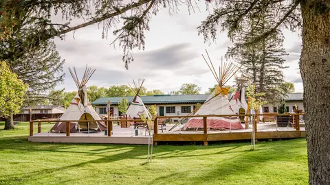 Several tipis are set up on a wooden deck outside a building.
