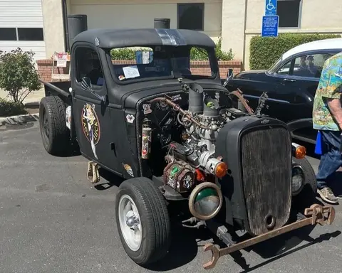 A custom black hot rod truck parked outdoors with an exposed engine.
