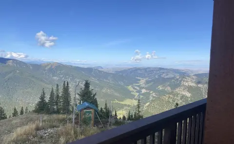 A scenic view of a mountain valley and hills from a balcony with a small outbuilding below.