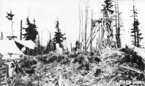 An old photograph showing a wooden tower structure and a tent in a wooded area.