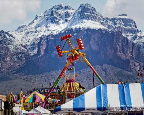 A carnival ride operates in front of a large snow-capped mountain range.