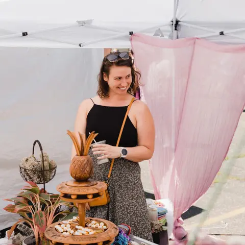 A smiling woman stands inside a tent with various items on display.