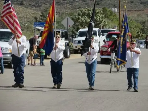 Four people carry flags in a parade down a street.