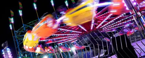 A colorful amusement park ride spins rapidly at night.