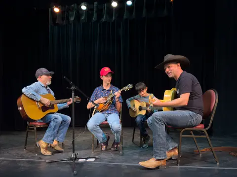 Four musicians play acoustic stringed instruments on a stage.