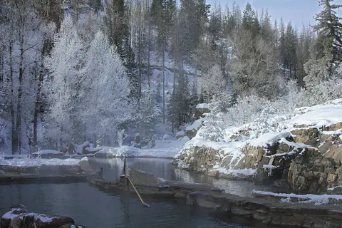 A hot spring pool surrounded by snow-covered trees and rocky landscape in winter.