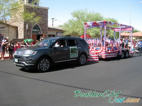 An SUV pulls a patriotic parade float with flags and banners.