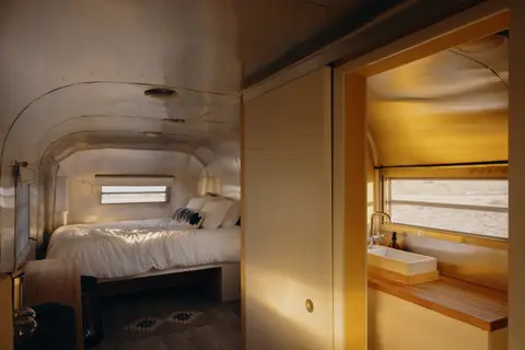 An interior view of a retro camper trailer showing a bedroom and a bathroom area.