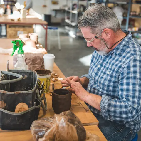 A man shaping a pottery piece in a workshop.