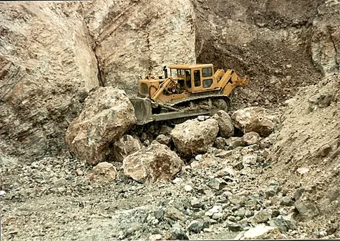 A bulldozer pushes large boulders in a rocky quarry.