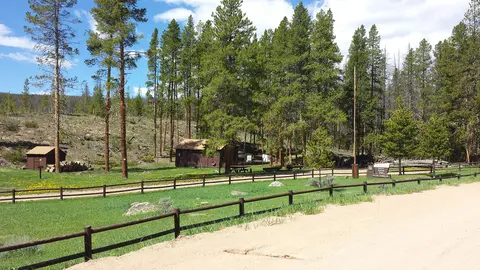 A forest landscape with cabins, a dirt road, and a wooden fence.