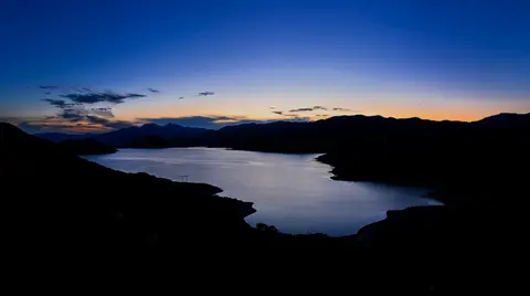 A wide view of a lake and dark silhouetted mountains during twilight.