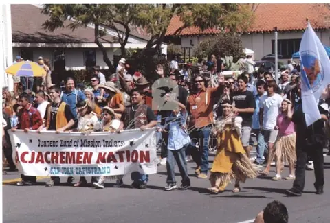 A crowd of people in a parade walking down a street carrying a banner and flags.