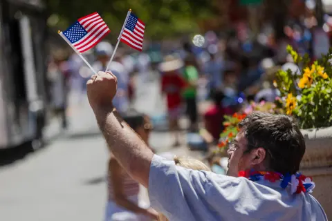 A person holds two small American flags during an outdoor event.