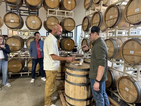 People taste wine from a barrel in a winery cellar.