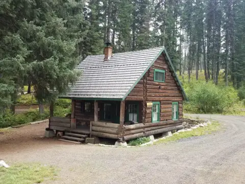 A log cabin stands in a wooded area near a dirt road.