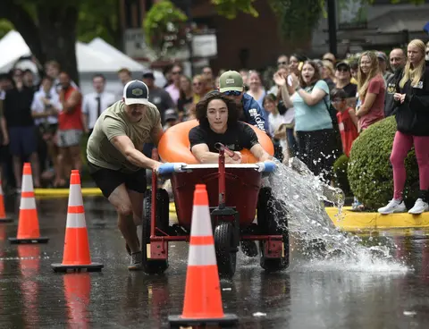 People participate in a street race with a water-filled cart, watched by a crowd.