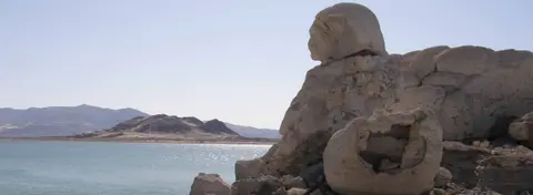 A large rock formation by the water with mountains in the background.