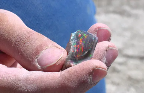 A hand holds a colorful opal gemstone.