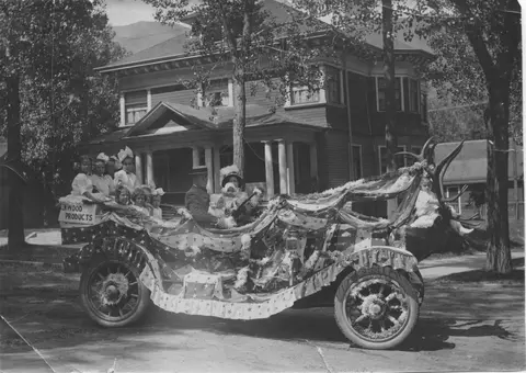 A historic black and white photograph showing a decorated parade vehicle carrying people.