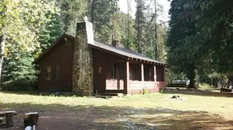 A wooden cabin with a stone chimney stands among trees.