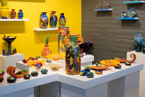 Colorful blown glass art pieces displayed on shelves and tables inside a shop.