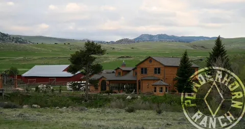 A log cabin ranch house with a red barn in a rural landscape.