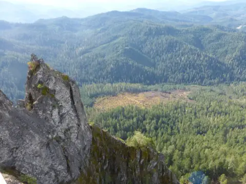 An elevated view of a rocky outcrop overlooking a forested mountain landscape.