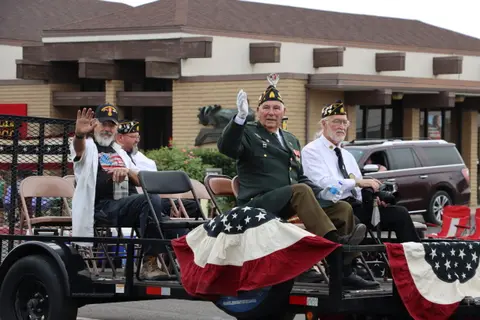 Several veterans ride on a trailer decorated with American flags in a parade.