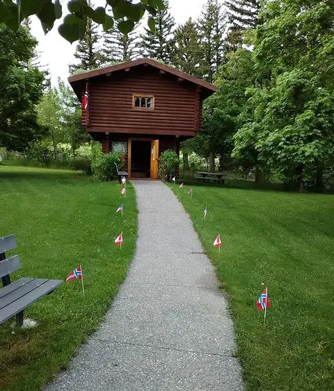 A concrete walkway leads toward a log building surrounded by green grass and trees.