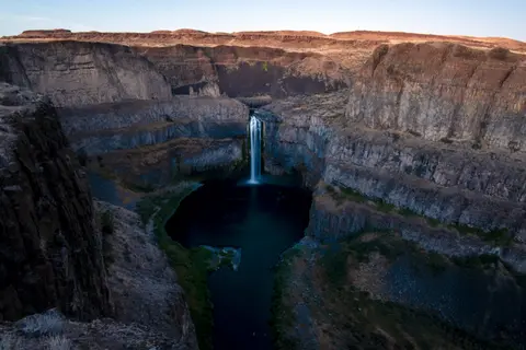 A waterfall cascades into a deep pool surrounded by steep canyon walls.