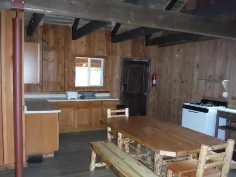 An interior shot of a rustic kitchen and dining area with wooden walls and exposed beams.