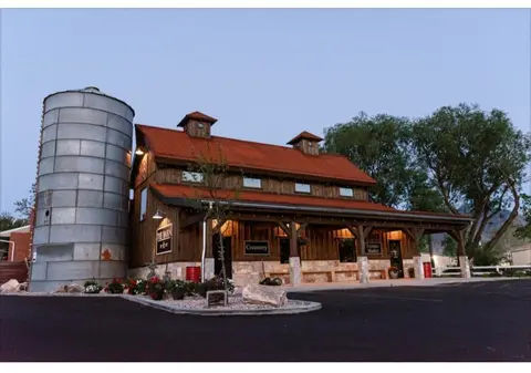 A rustic barn building with a metal silo stands outside at dusk.