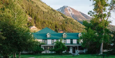 A large white building with a green roof stands before a mountain range.