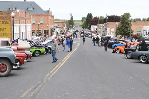 Classic cars line both sides of a town street during an outdoor event.
