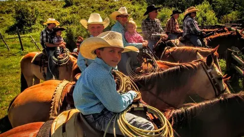 A group of people wearing cowboy hats riding horses outdoors.