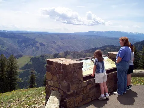 Three people look at an interpretive sign overlooking a mountain valley landscape.
