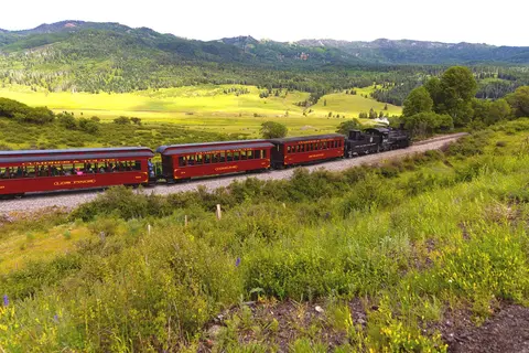 A steam train travels through a mountainous landscape.