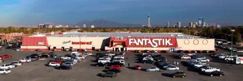 An exterior view of a large building with a parking lot and a city skyline in the distance.