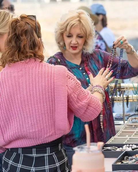 A woman looks at beaded necklaces displayed at an outdoor market stall.