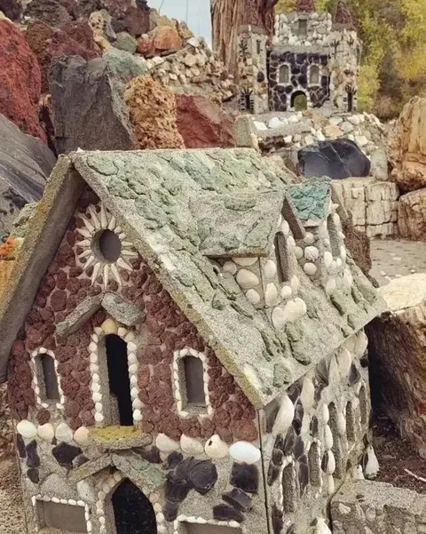 A small decorative stone house stands in a rocky outdoor landscape.