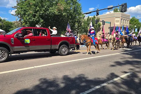 A parade on a street with a red pickup truck and people on horseback.