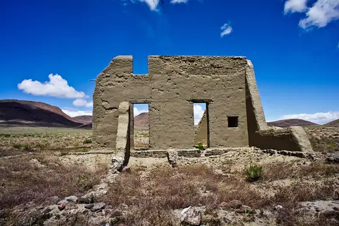 An old adobe ruin stands in a dry landscape under a blue sky.