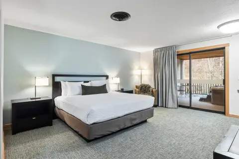 A modern hotel bedroom interior with a large bed and a balcony view.