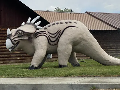 A large dinosaur statue stands outside a wooden building.
