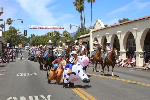 A parade on a street featuring people on horses and in inflatable costumes.