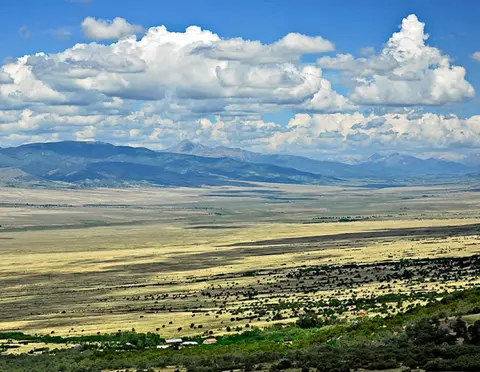 A wide landscape view of a vast valley with mountains in the background under a cloudy blue sky.