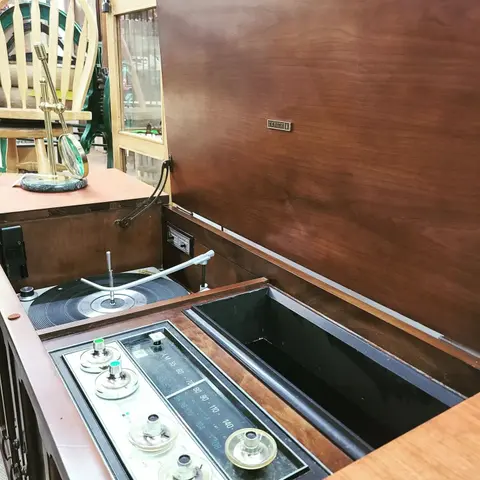 A vintage wooden stereo console with the lid open showing a turntable and radio dial.