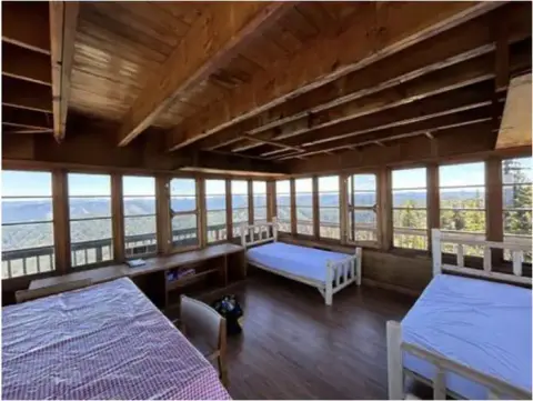 An interior view of a rustic room with wooden walls and beds surrounded by windows.
